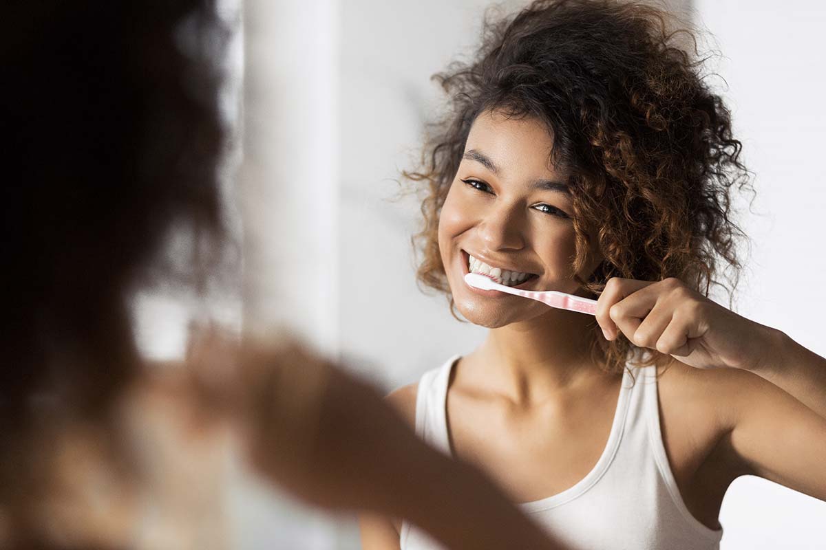 young girl brushing her teeth in the mirror to start maintaining your oral health