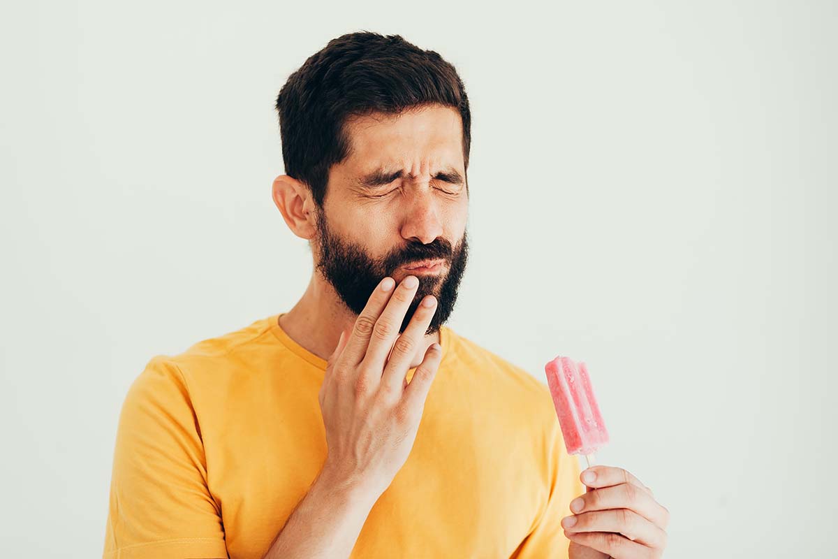 man wincing in pain and holding jaw from popsicle cold needing to learn, what are cavities