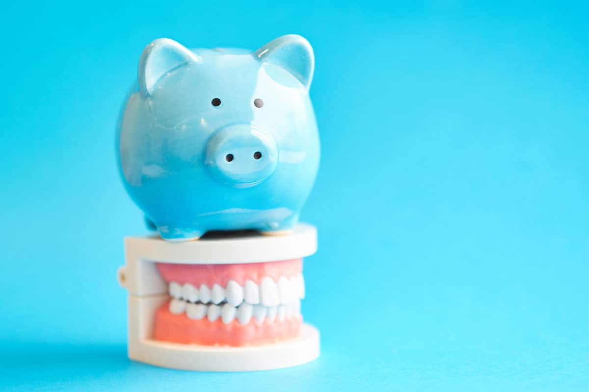 a piggy bank on top of dentures illustrating how much do dentures cost